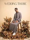 Muslim man wearing a grey wedding thobe seated on a stool surrounded by flowers — Furqanwear