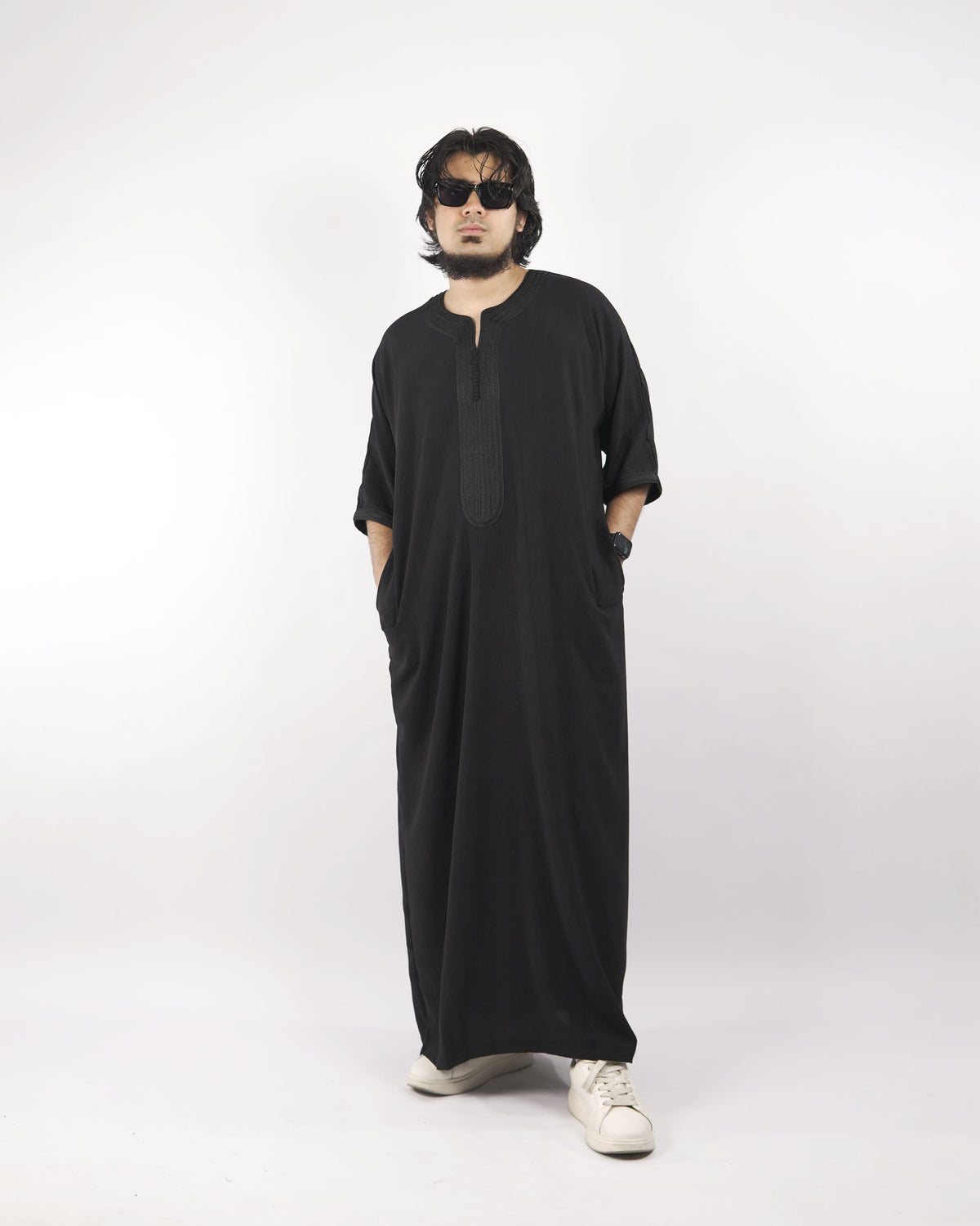 Model wearing a black half sleeve Moroccan thobe, full length front view, with sunglasses and white sneakers, against a plain white background.