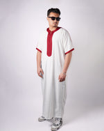 Man standing wearing a full-length white thobe with short sleeves and maroon embroidered trim.
