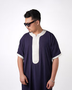 Man wearing sunglasses looks to the side while modelling a navy blue short-sleeve gandoura featuring light grey contrast trim.