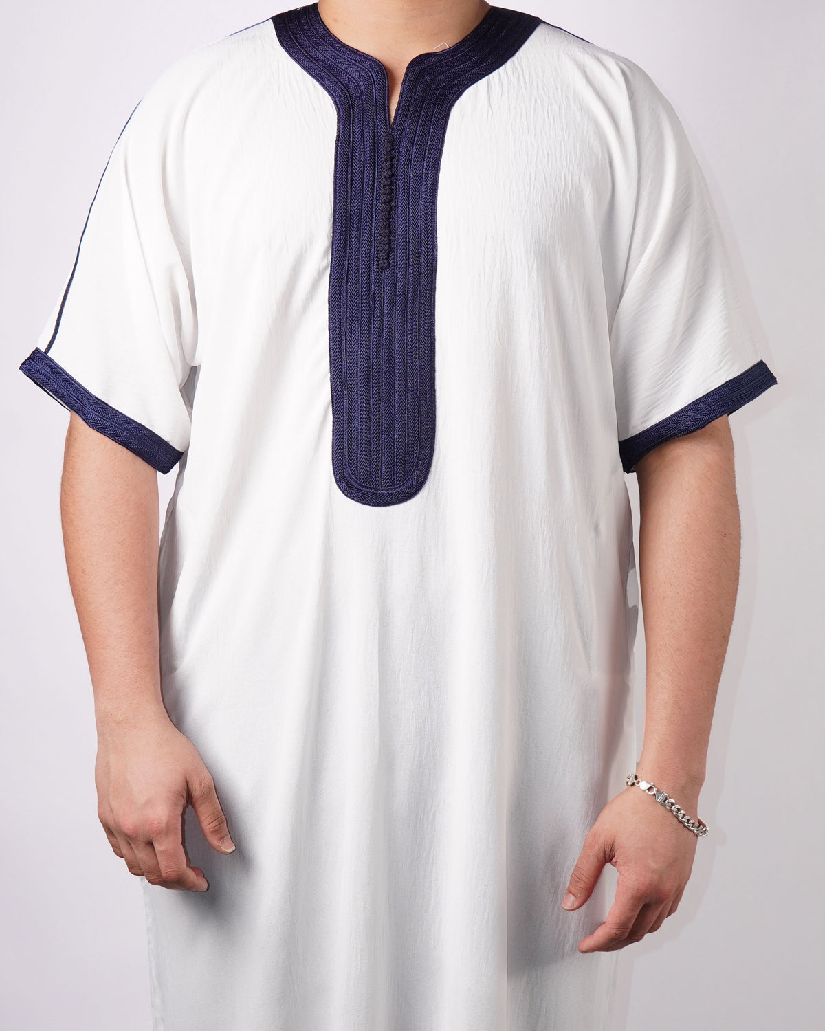 Close-up showing the navy blue embroidered trim on the neckline, placket, and cuffs of a men's white short-sleeve thobe.