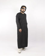 Man models a black classic thobe, full length view, showcasing it as stylish islamic clothing for men.