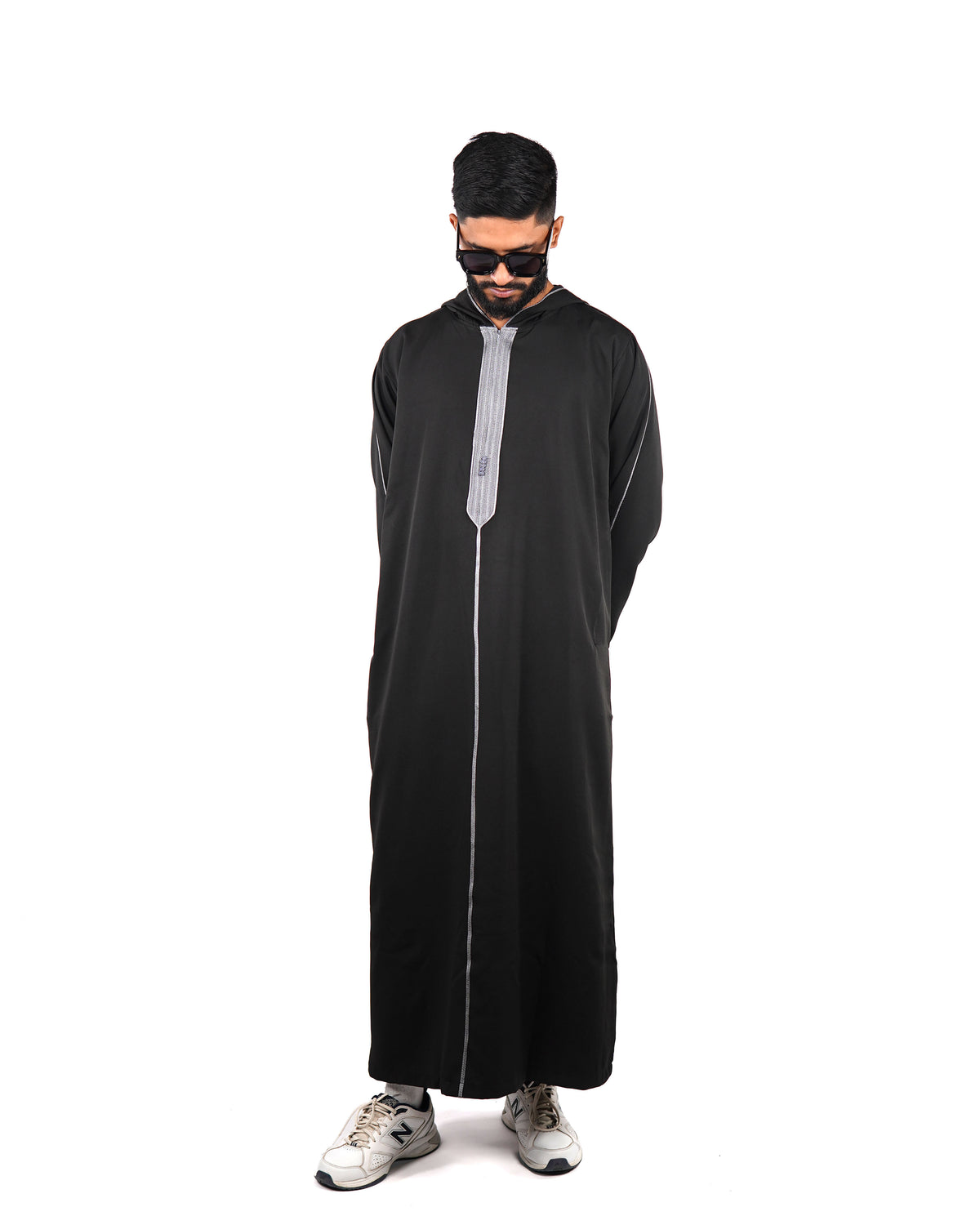  Man standing full length wearing a men's hooded black thobe with silver trim, hands behind back.