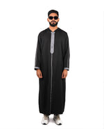 Front view, full length, of a man looking forward wearing a hooded black thobe with silver trim.
