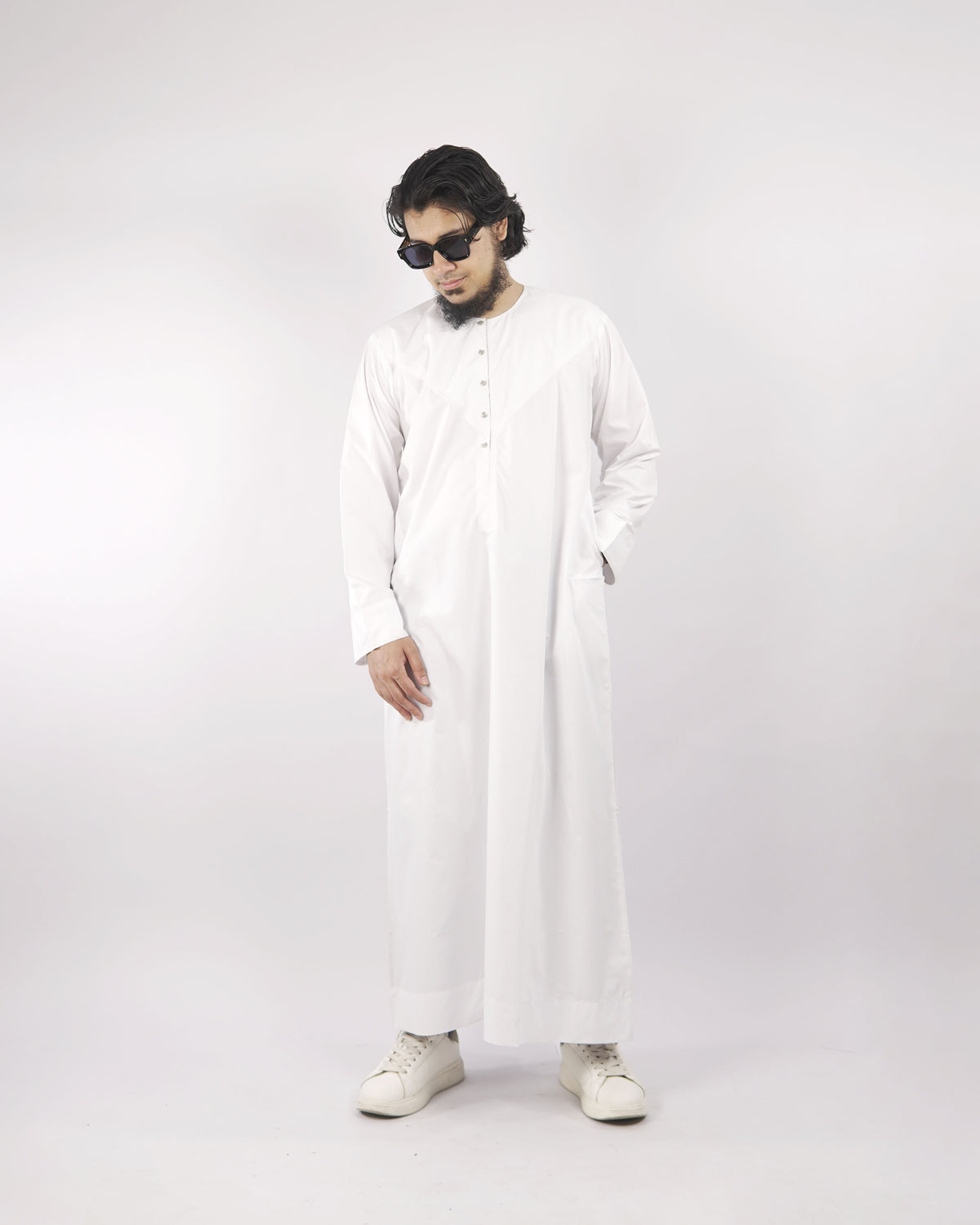 Man models a classic white men's thobe jubba, standing angled with hand in pocket, a versatile piece of Islamic clothing for men.