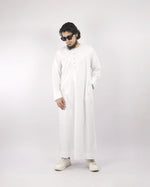 Man models a classic white men's thobe jubba, standing angled with hand in pocket, a versatile piece of Islamic clothing for men.